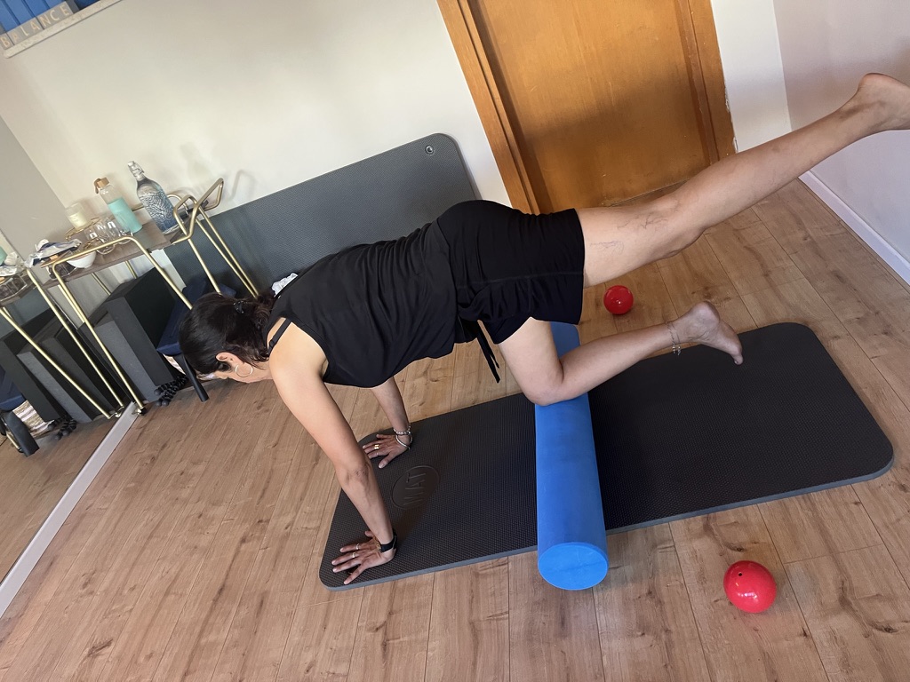 מתאמנת בהרמת רגל עם גליל פילאטיס כחול בשיעור בסטודיו